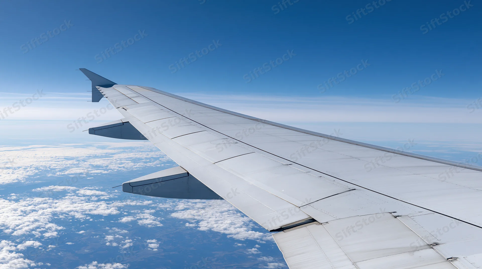 Airplane wing extending into blue sky above scattered clouds viewed from passenger window during flight