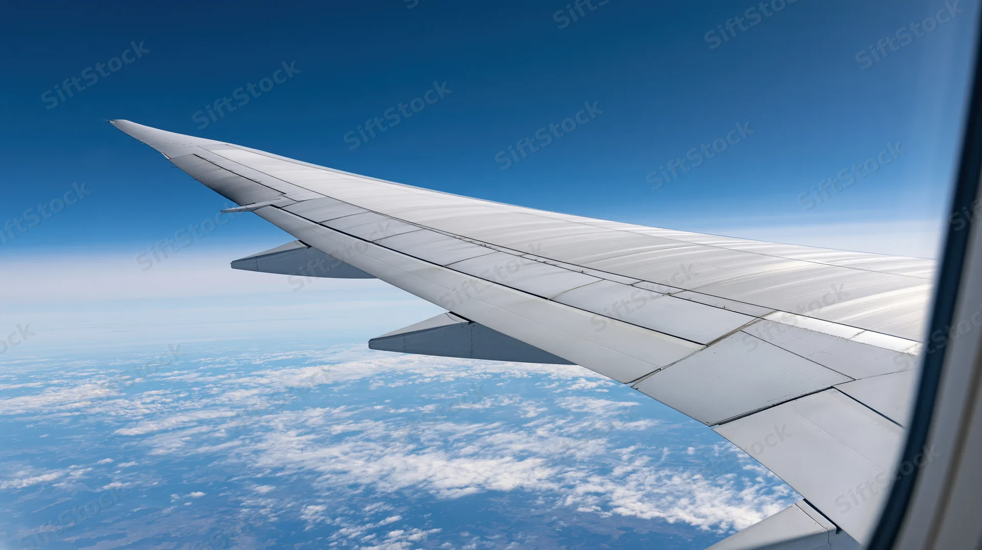 Airplane wing viewed through passenger window above clouds during flight