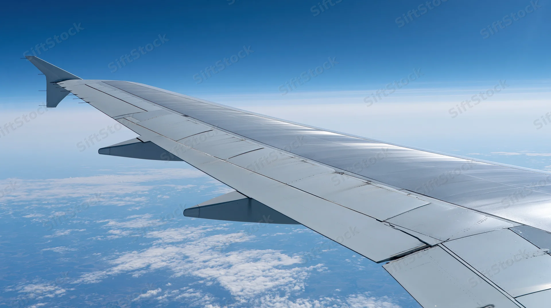 Airplane wing viewed from passenger window during flight above clouds
