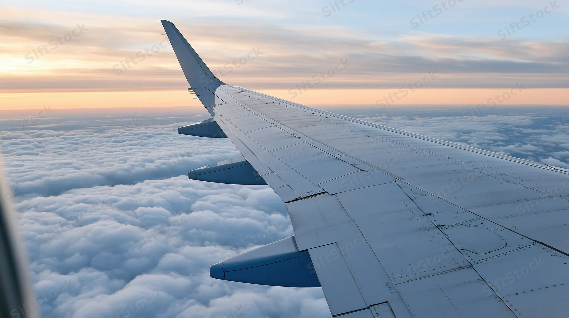 Airplane wing extending over cloud layer during sunset viewed from passenger window