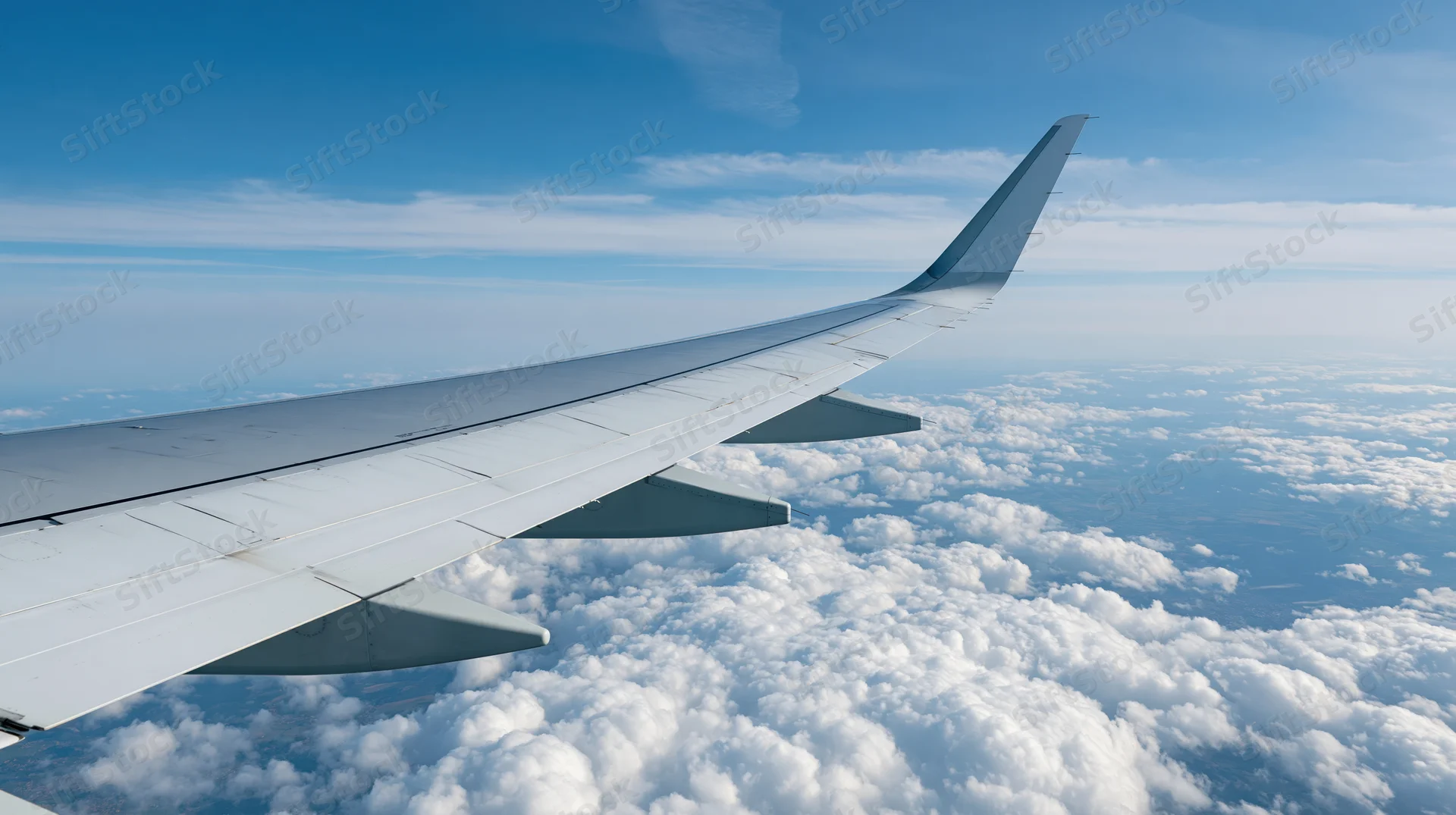 Airplane wing extending over fluffy white clouds viewed from passenger window during cruising flight