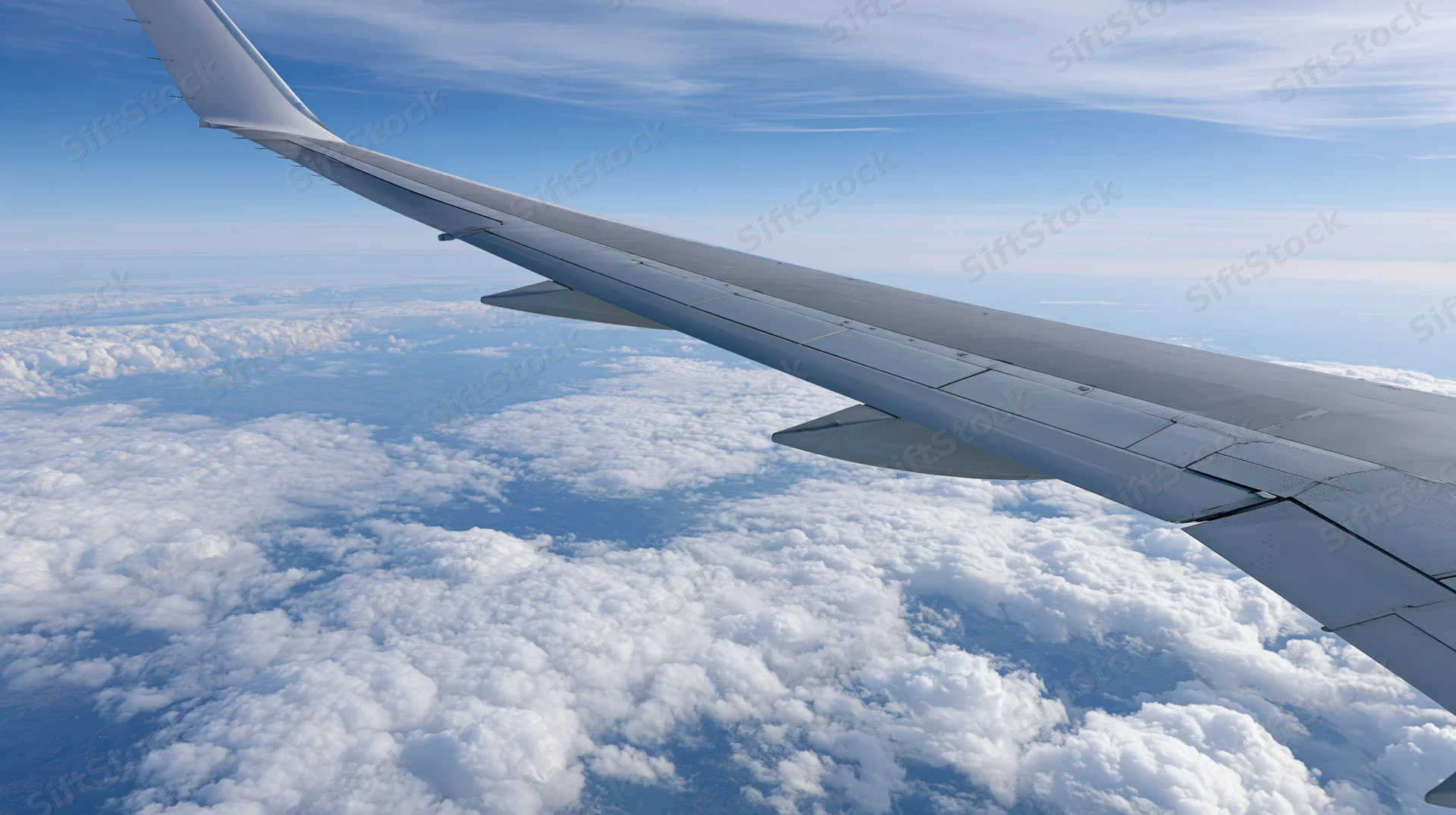 Airplane wing extending over a sea of clouds viewed from passenger window during cruising flight