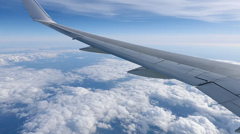 Airplane wing extending over a sea of clouds viewed from passenger window during cruising flight