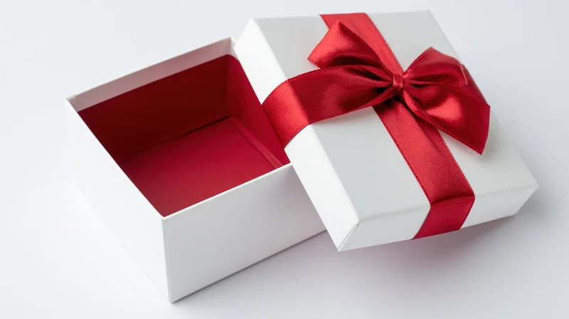 Open white gift box with red ribbon bow on plain white surface