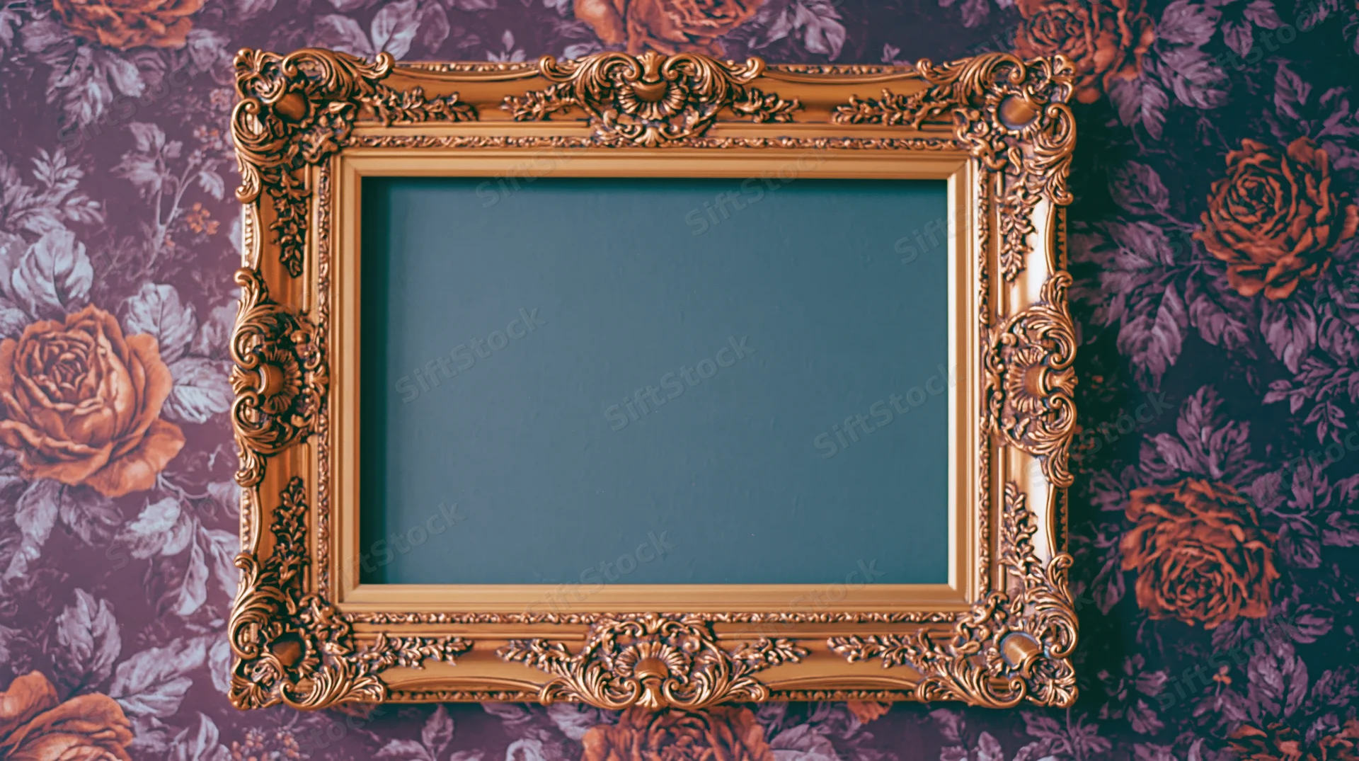 Ornate gold baroque frame with carved detailing hanging on floral wallpapered wall
