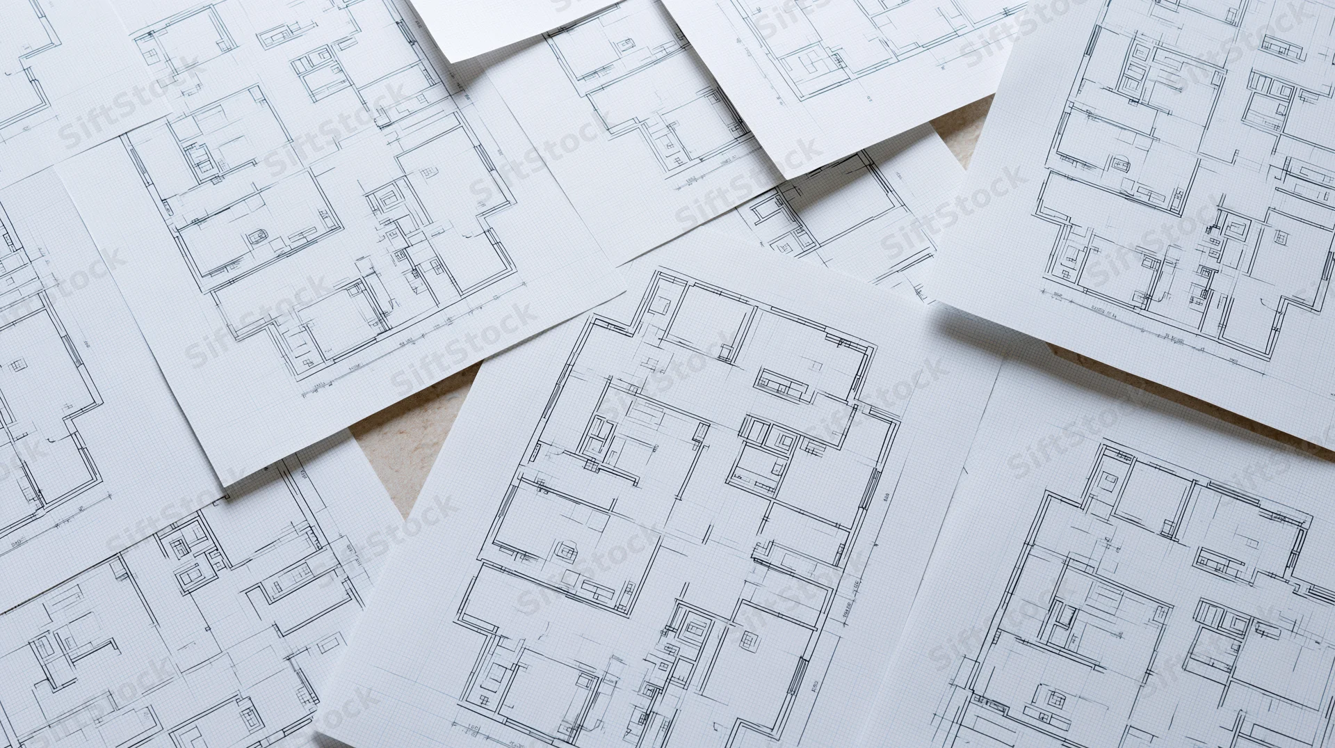 Architectural floor plans printed on white graph paper scattered on a surface