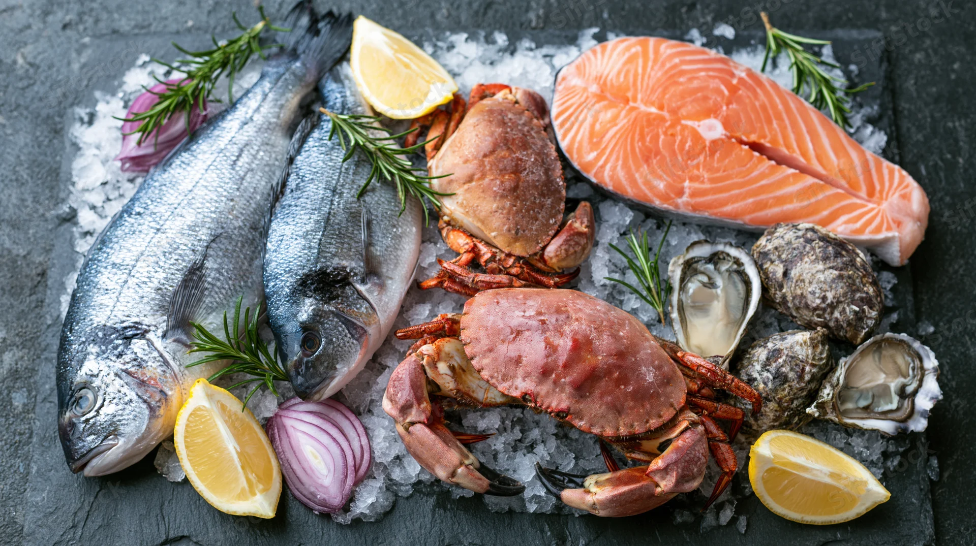 Assorted raw seafood including fish, crab, oysters and lemon on crushed ice on slate surface