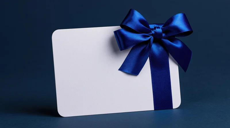 Blank white gift card with blue satin ribbon bow standing upright on dark blue surface
