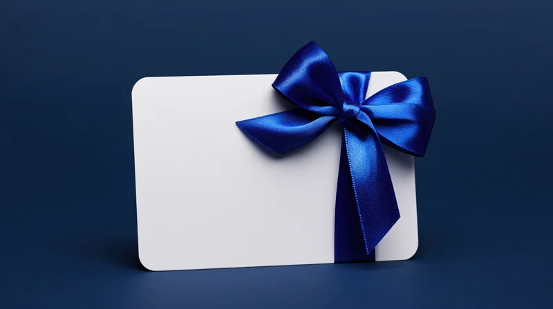 Blank white gift card with blue satin ribbon bow standing upright on dark blue surface