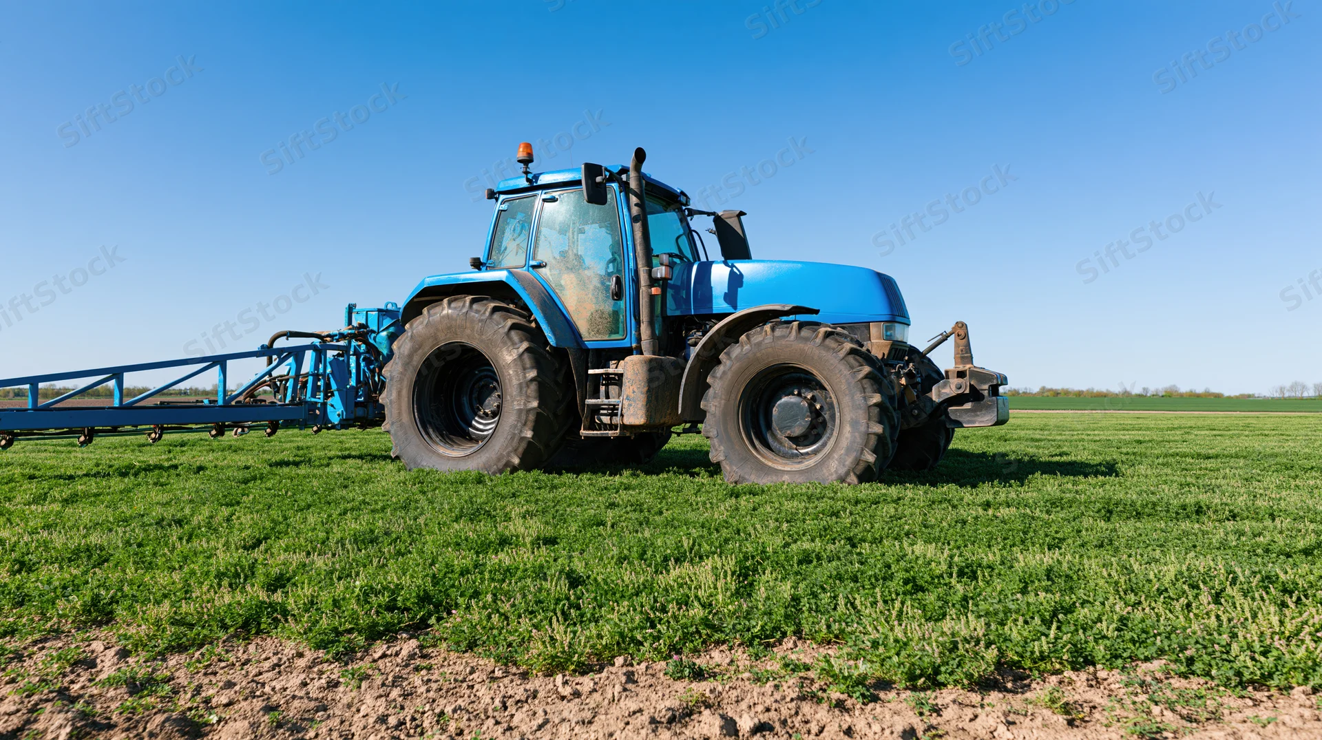 Blue tractor pulling spray boom across green field