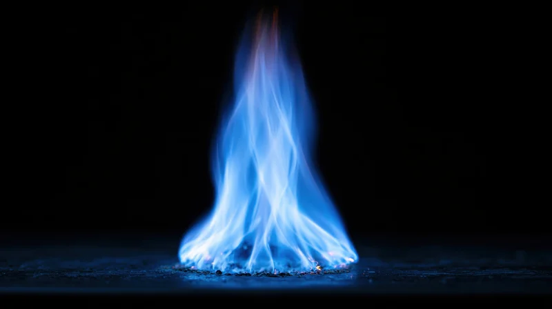 Blue gas flame burning in darkness on a dark surface