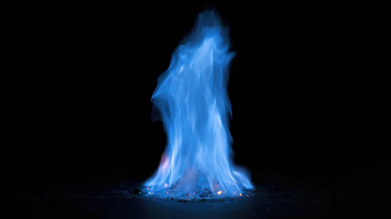 Blue gas flame burning intensely in near-darkness against a black background
