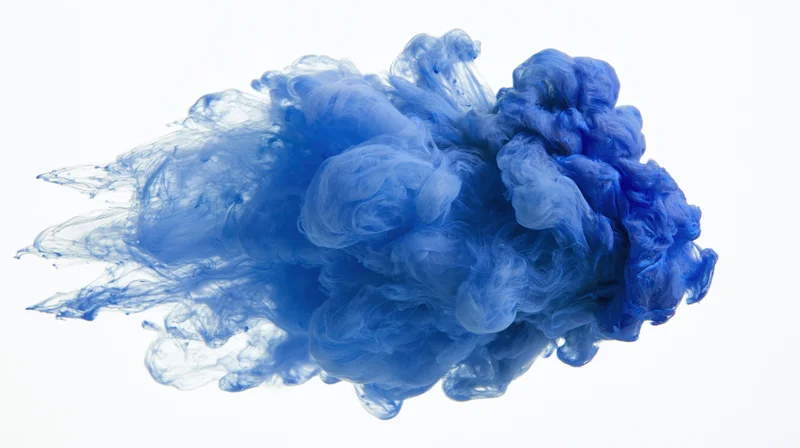 Blue ink dissolving and billowing in water against white background