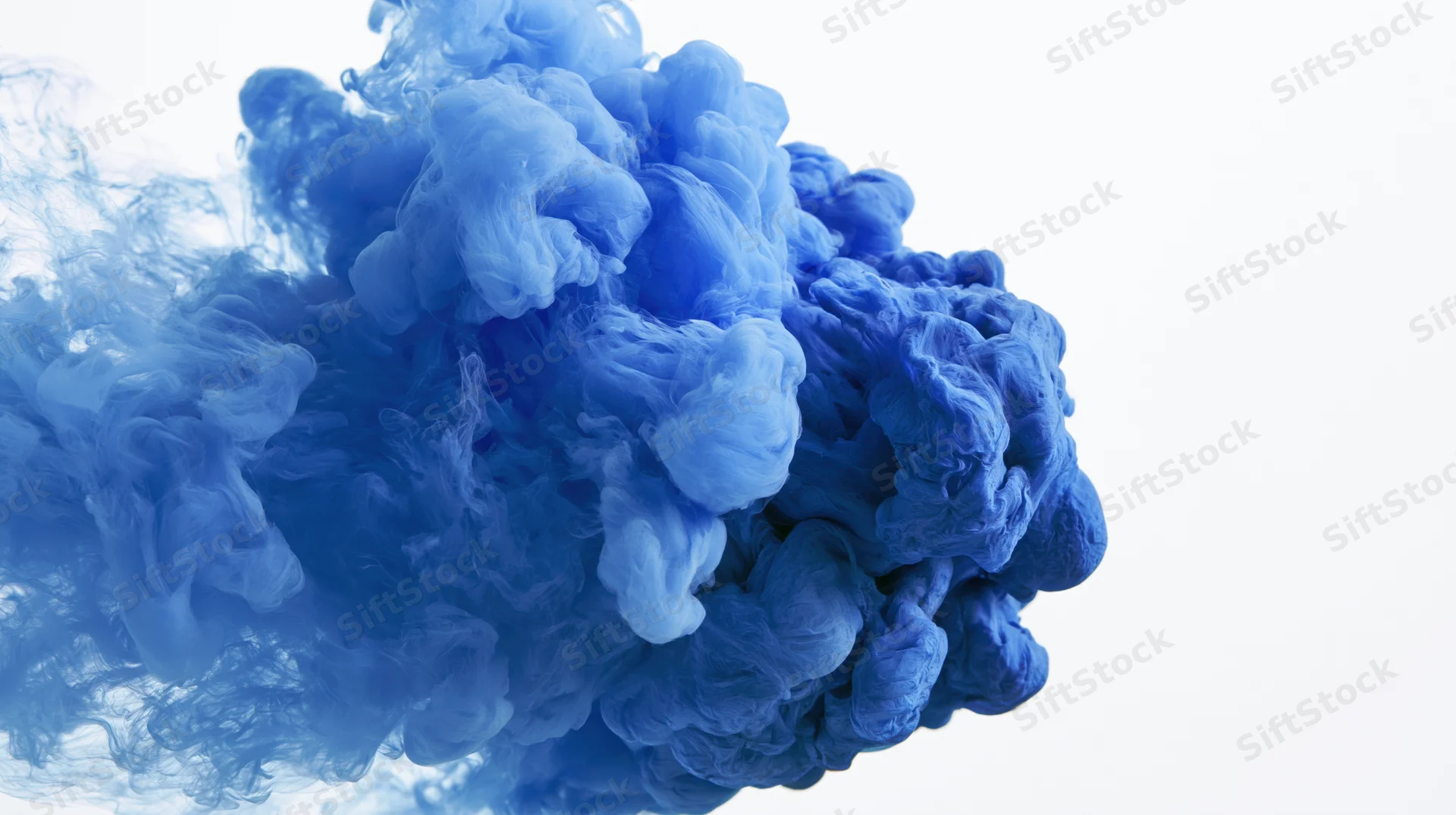 Blue ink dissolving and billowing in water against white background