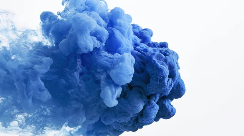 Blue ink dissolving and billowing in water against white background