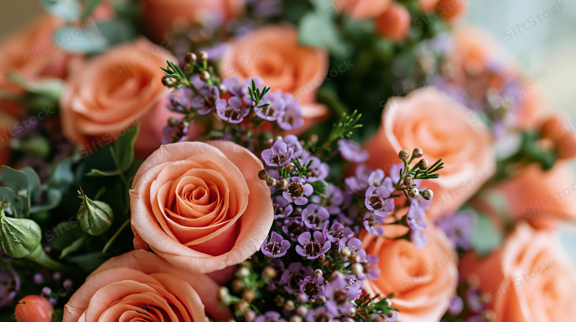 Close-up of a salmon-pink rose bouquet with purple filler flowers and greenery