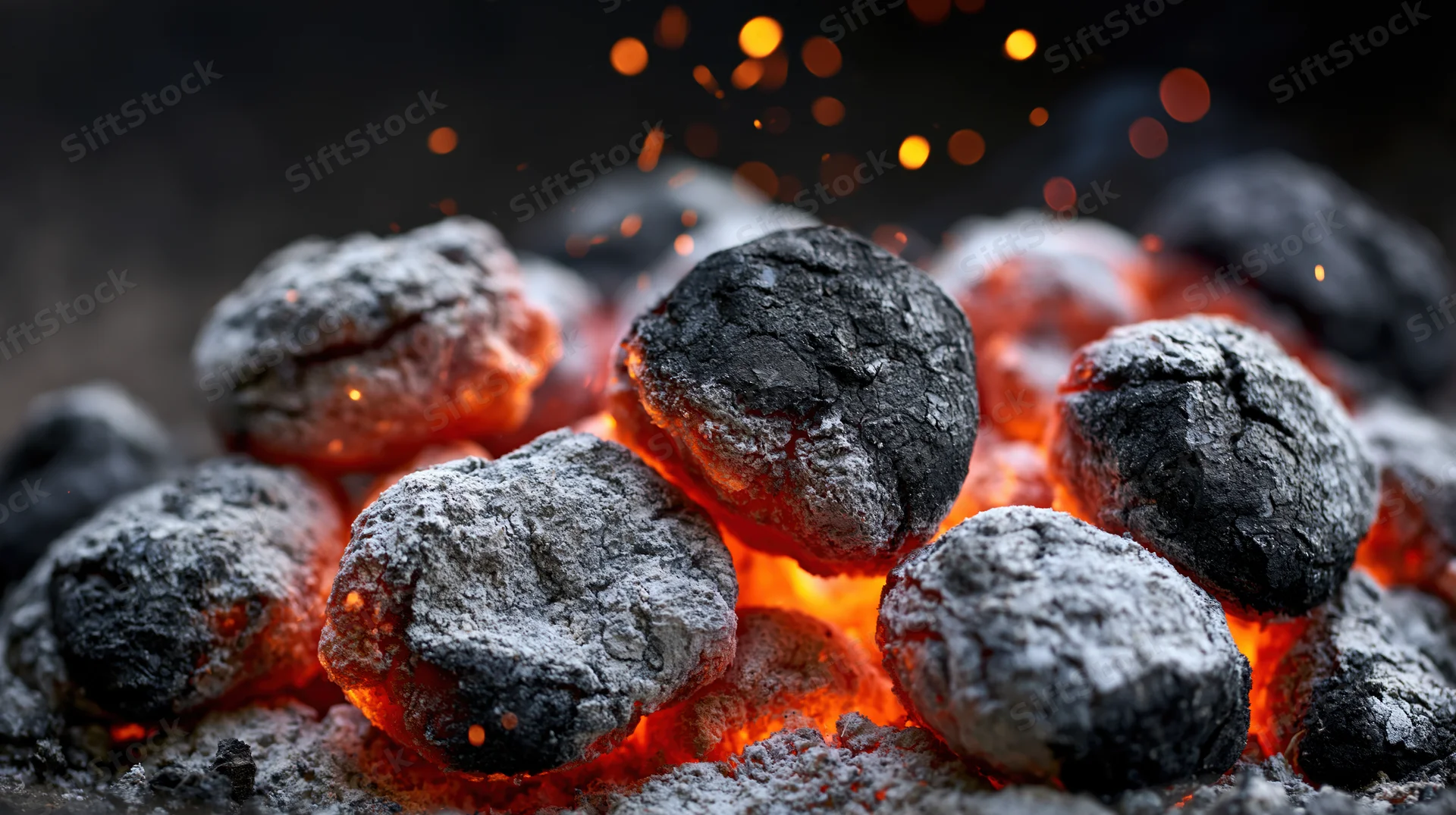 Glowing charcoal briquettes with sparks in a grill pit at night