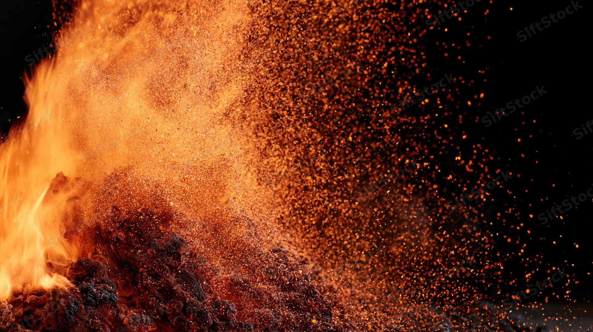 Close-up of flames bursting upward with glowing sparks against black background