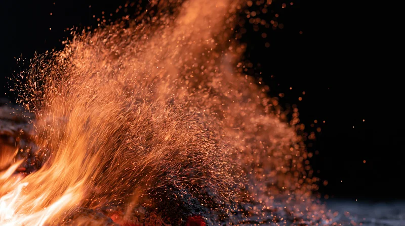 Close-up of flames bursting upward with glowing sparks against dark background