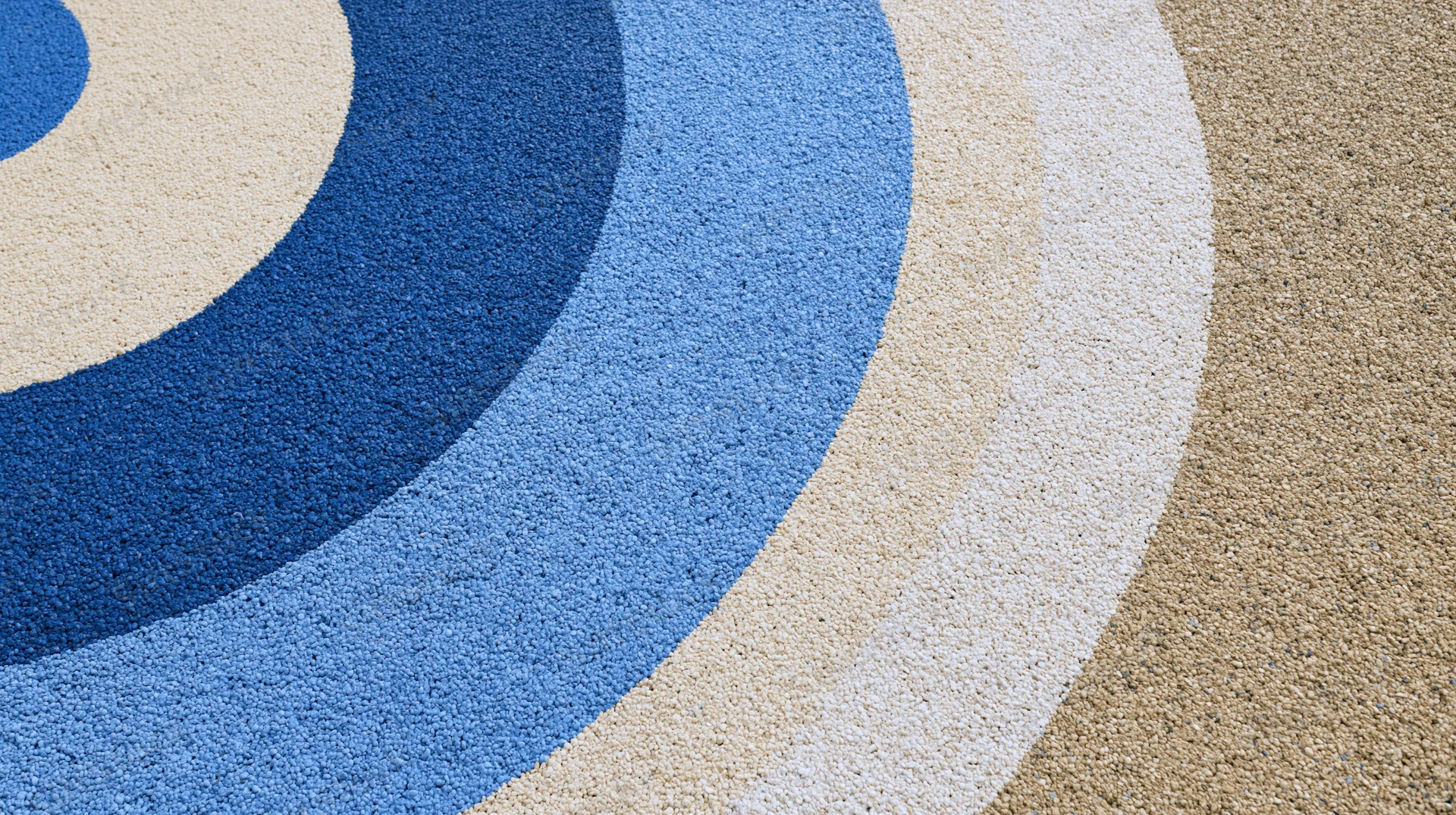 Close-up of circular patterned rubber playground surface with blue and beige concentric circles