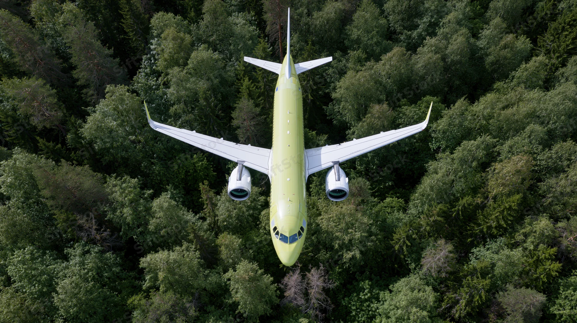 Commercial passenger airplane in lime green livery flying overhead above dense forest canopy