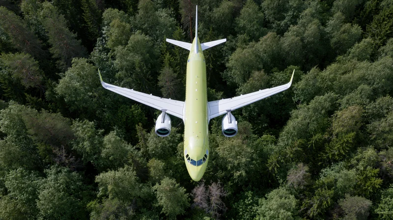 Commercial passenger airplane in lime green livery flying overhead above dense forest canopy