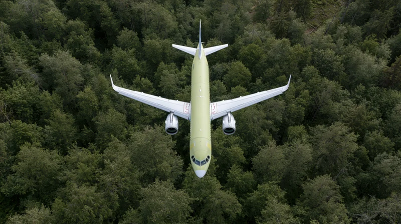Commercial passenger airplane in lime green livery flying over dense forest canopy