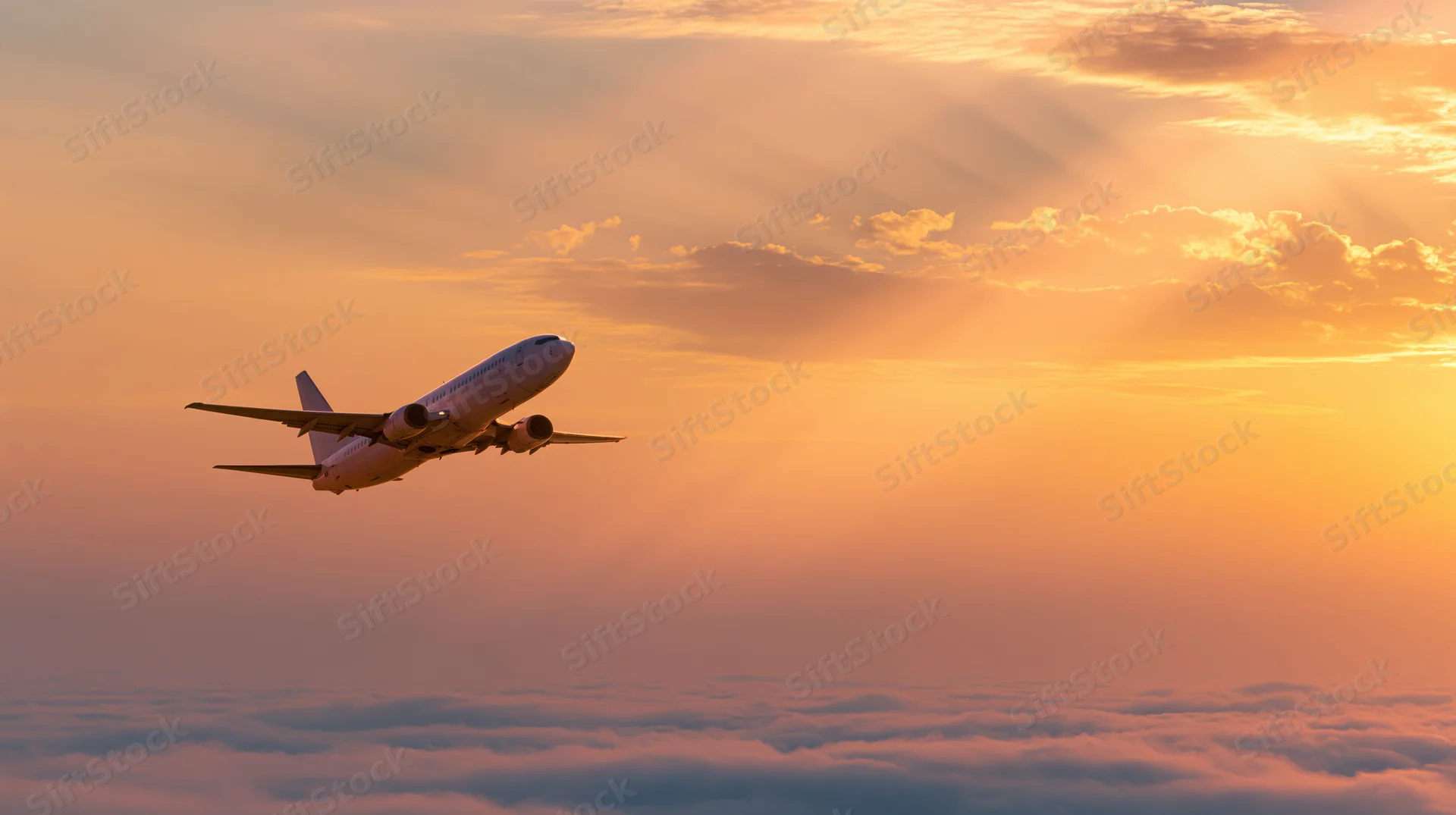 Commercial passenger jet climbing above cloud layer at sunset