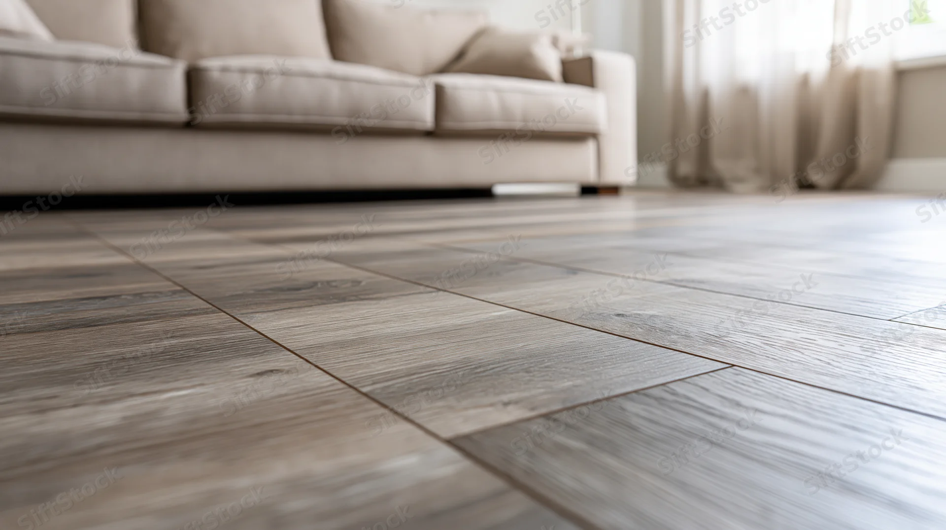 Close-up of dark grey-brown hardwood floor planks in a living room with beige sofa and curtains in background