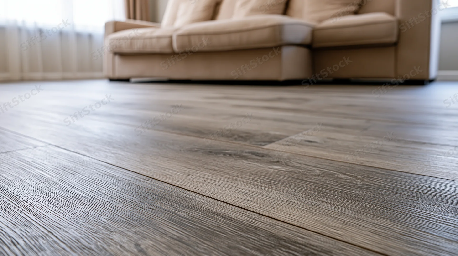Dark grey-brown hardwood floor planks in sharp focus filling foreground with beige sofa in background