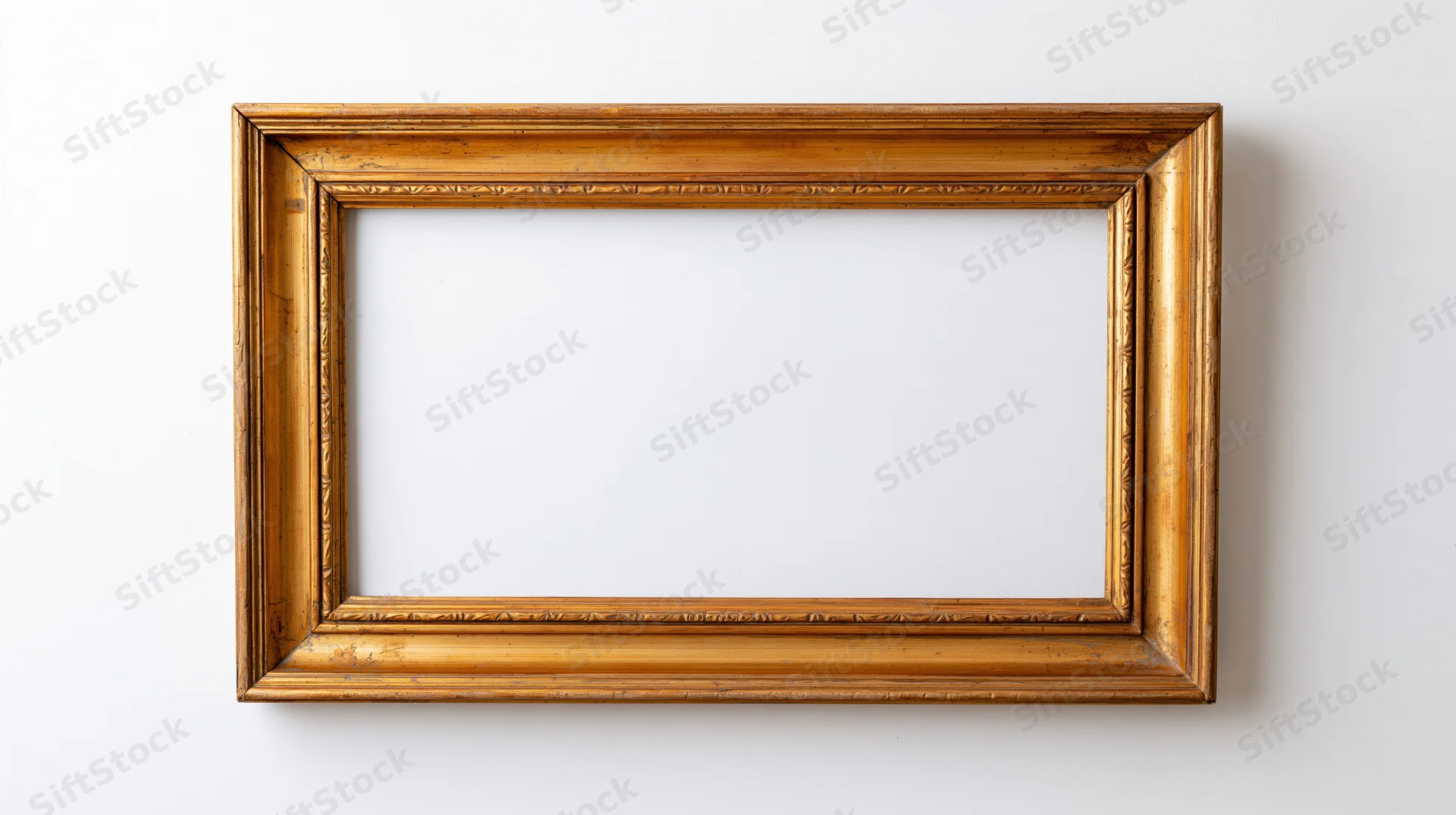 Empty antique gold picture frame with ornate molding hanging on a white wall