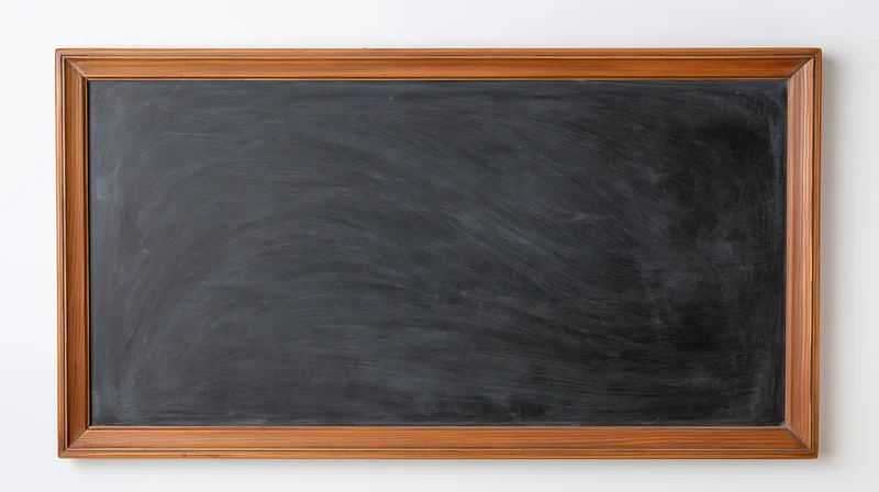 Empty blackboard with faint chalk smudges and eraser marks mounted on a white wall
