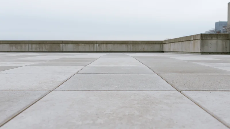 Wide concrete plaza floor with large square tiles extending toward a low wall under an overcast sky