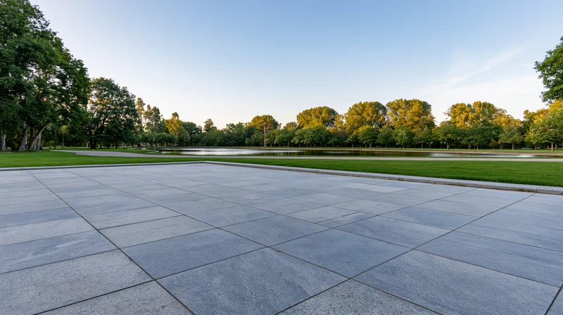 Stone tile plaza extending toward a pond surrounded by trees in a park