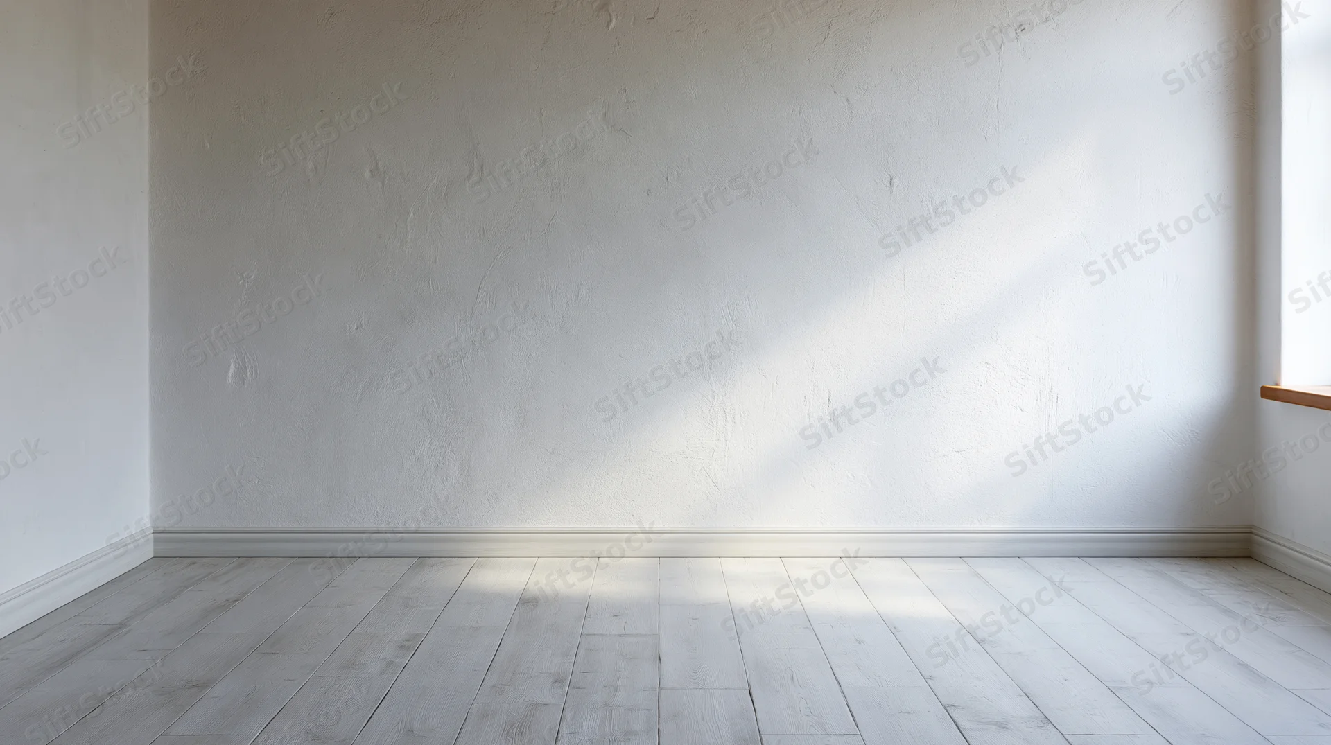 Empty room with white plaster wall and light wood floor, sunlight streaming in from window corner
