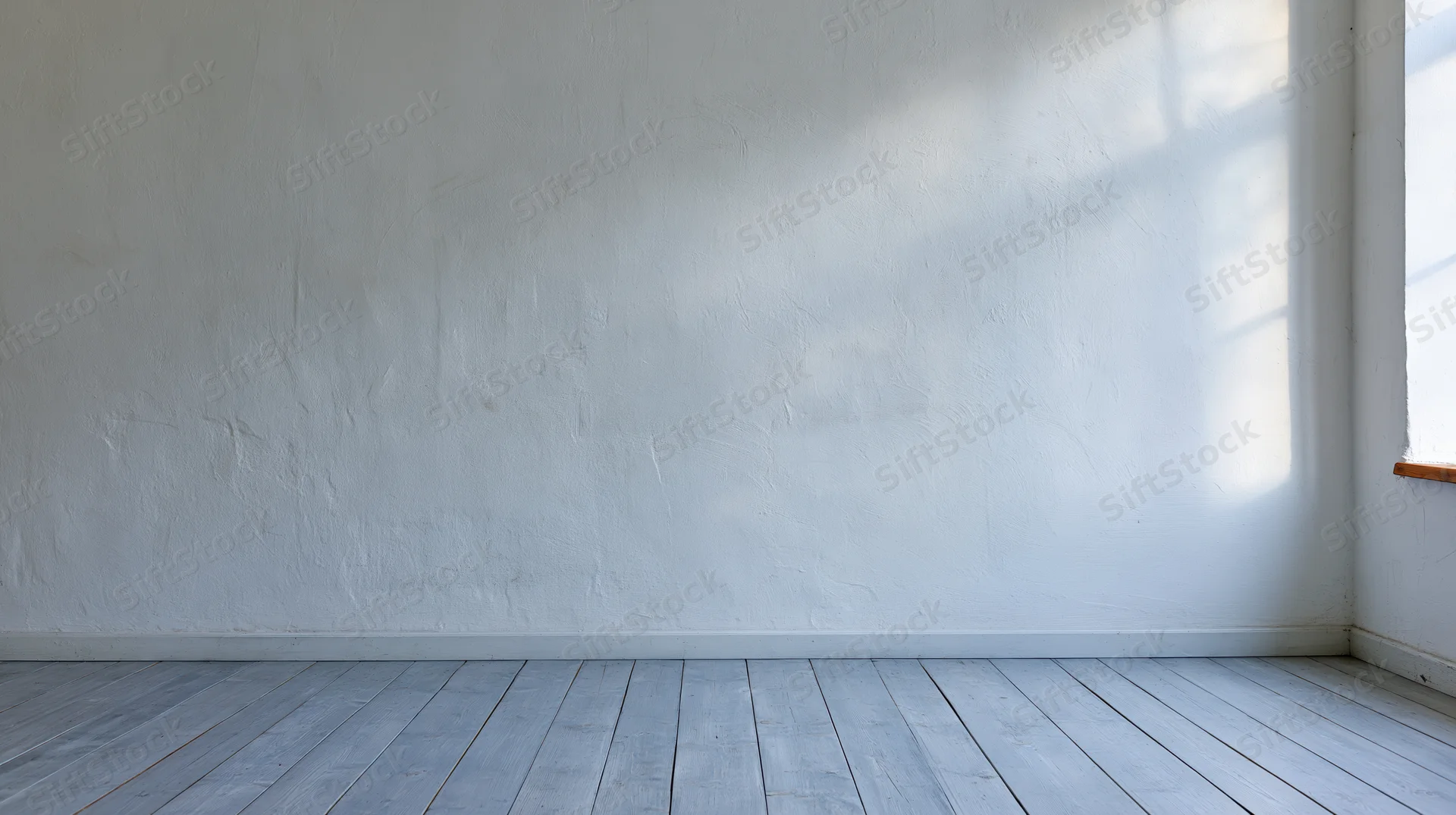 Empty room with white plaster wall and wooden floor lit by natural light from window