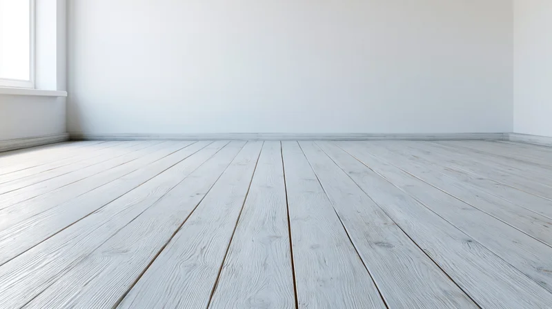 Empty room with whitewashed wooden plank floor and white walls, viewed from low angle near window