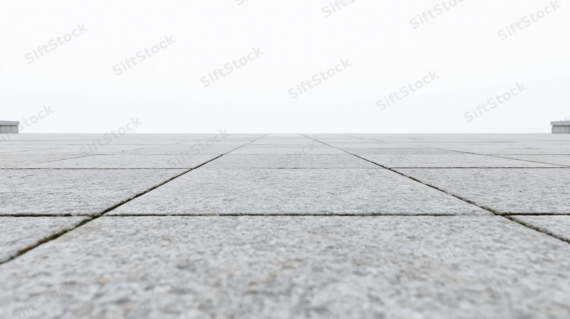 Low-angle view of light grey concrete tiles receding into the distance on an outdoor pavement