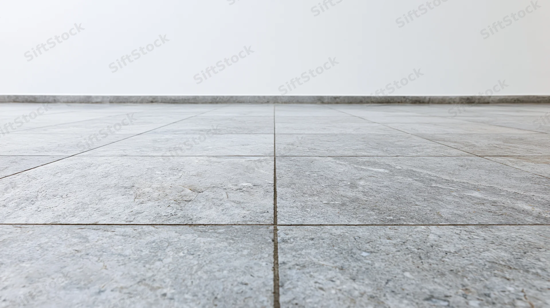 Light grey stone tile floor extending toward a plain white wall in an empty interior space