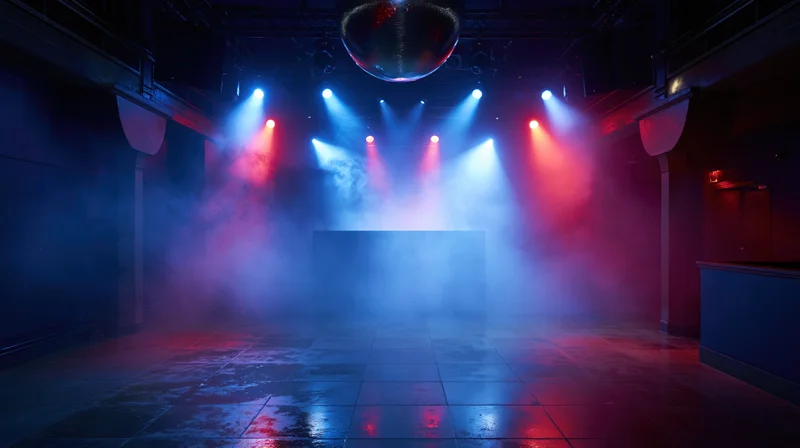Empty nightclub dance floor with dj booth at far end under colorful spotlights and smoke