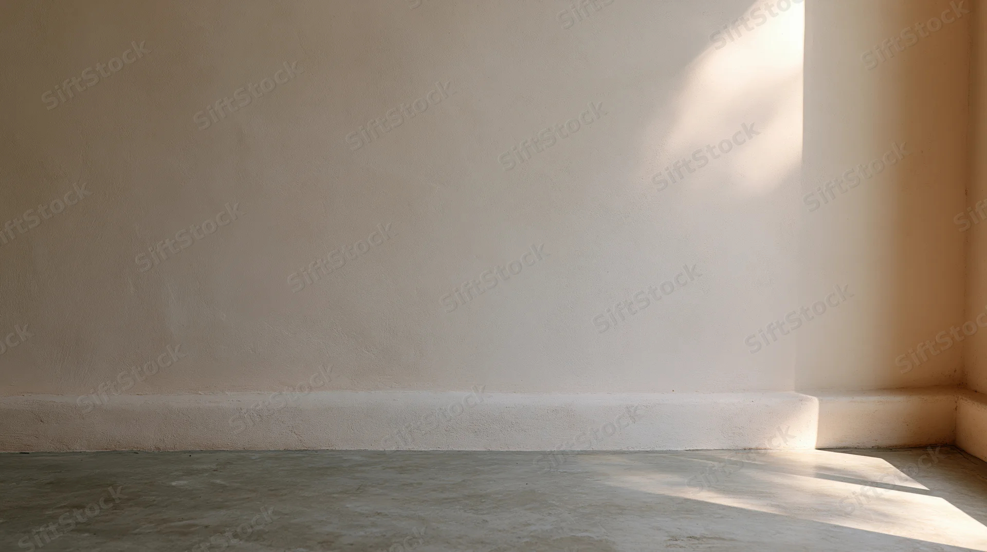 Empty room interior with bare plaster wall and concrete floor, sunlight casting shadows in corner