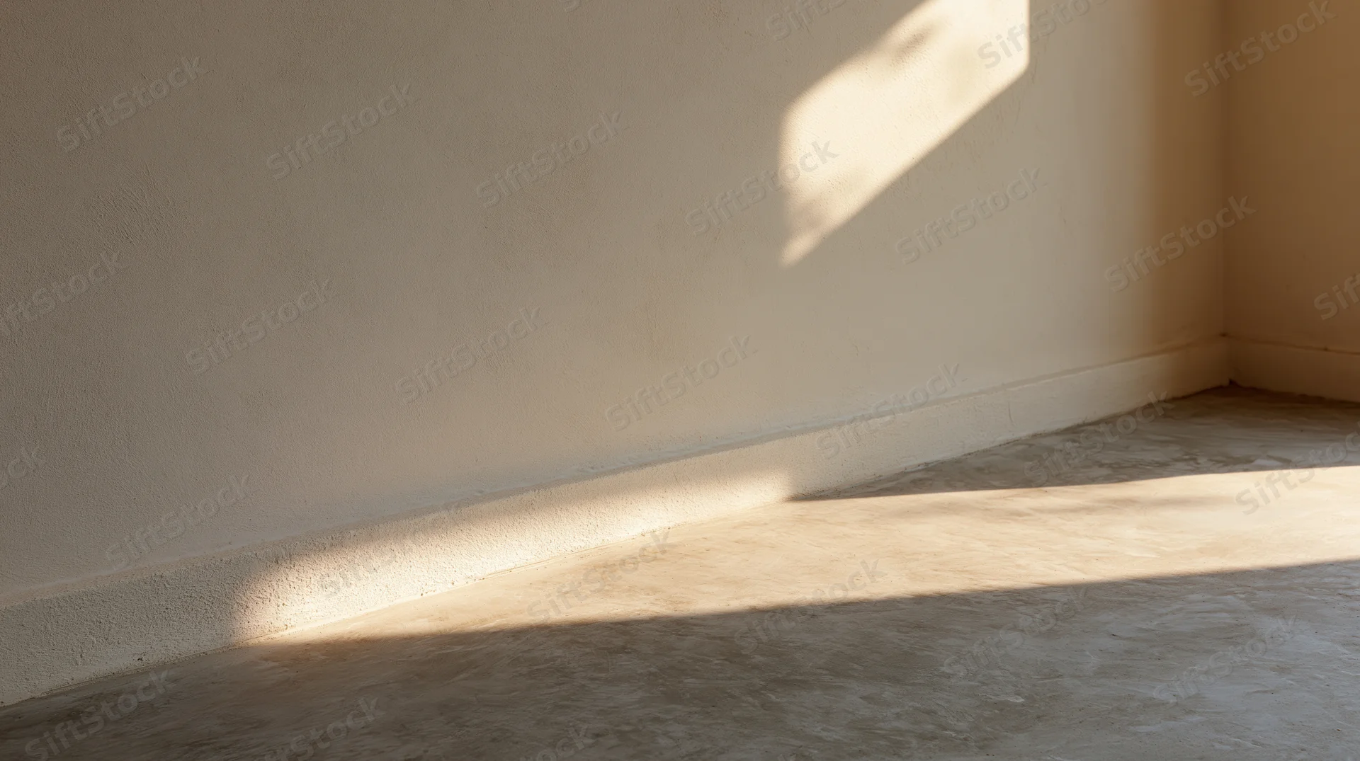 Empty room interior with bare plaster wall and concrete floor lit by natural sunlight casting shadows in corner