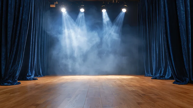 Empty theater stage with blue velvet curtains and spotlights casting beams through fog over polished hardwood floor