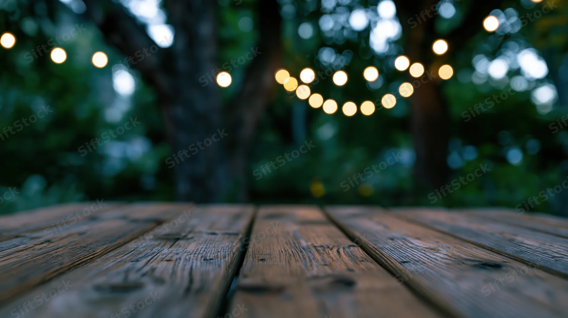 Weathered wooden deck surface in a garden at twilight with string lights in the background