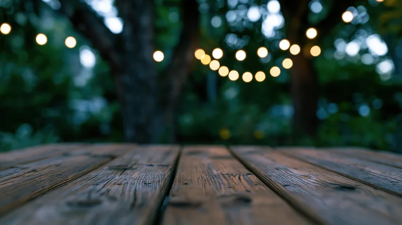 Weathered wooden deck surface in a garden at twilight with string lights in the background