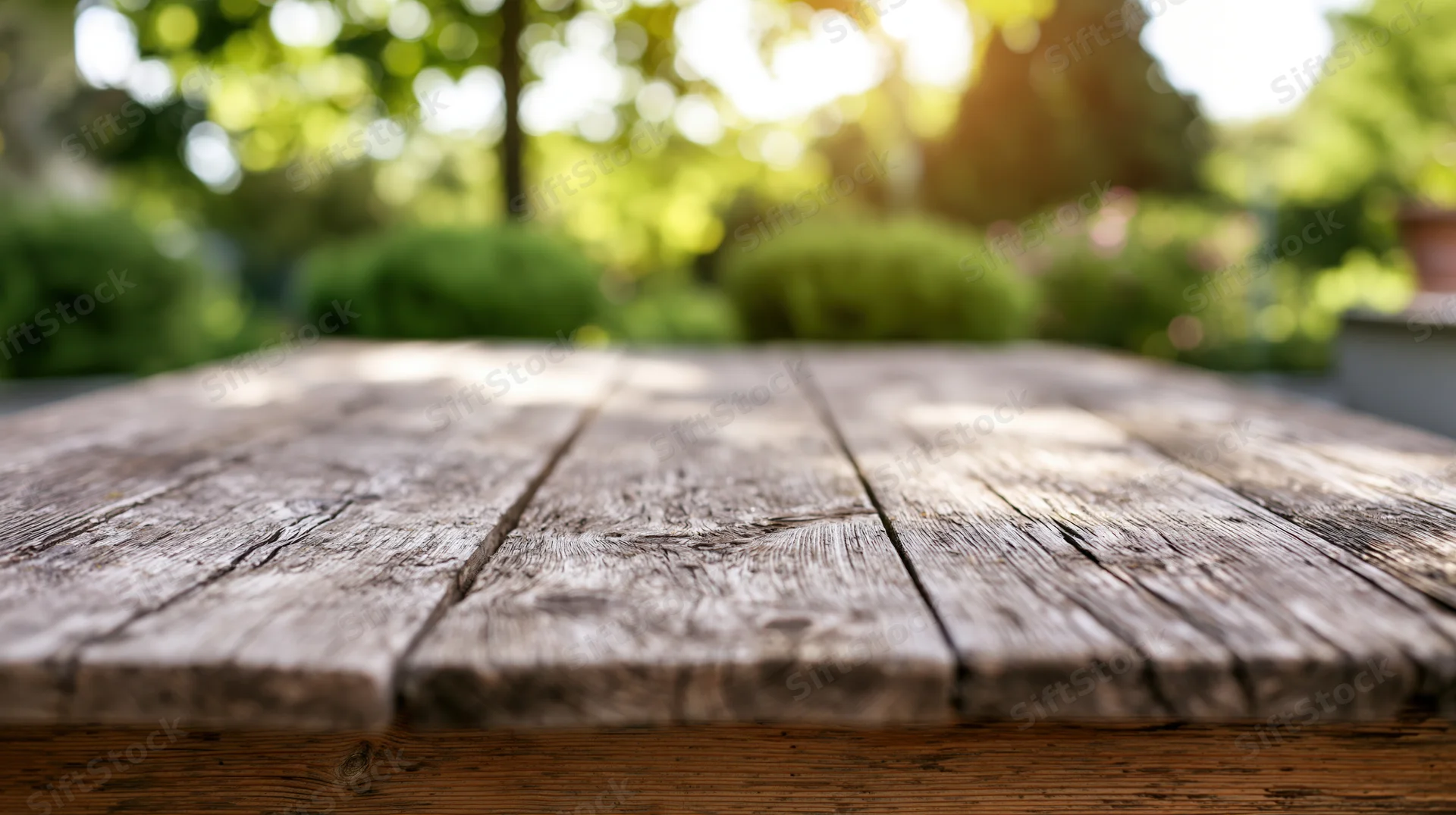 Weathered wooden table surface in sharp focus with blurred garden greenery and sunlight in background
