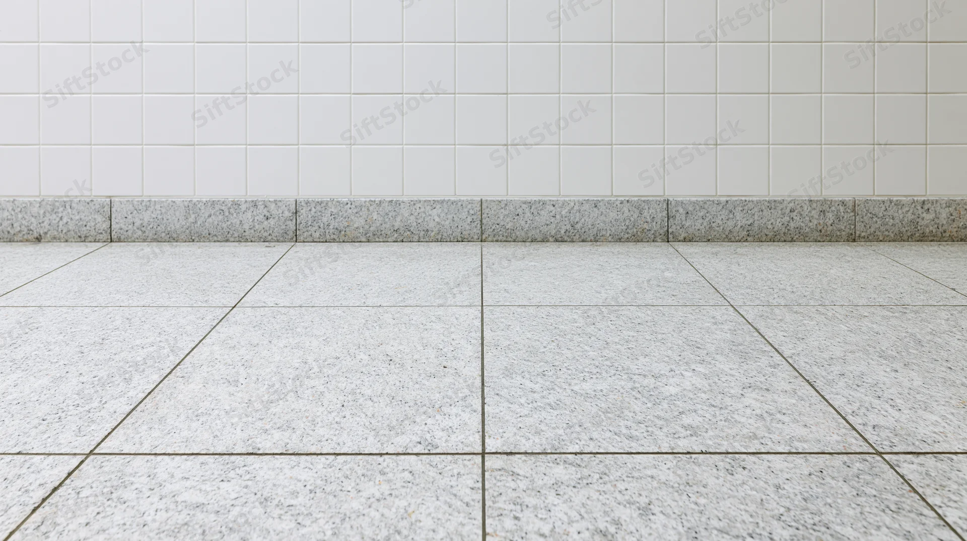 White granite tile floor meeting a white square-tiled wall in an empty interior space
