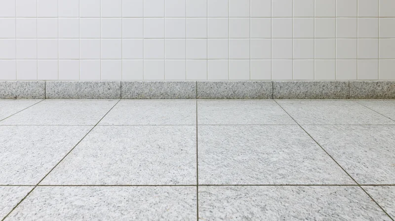 White granite tile floor meeting a white square-tiled wall in an empty interior space