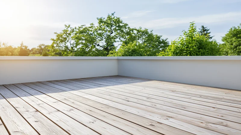 Empty wooden deck terrace with bleached planks and white walls overlooking green trees under bright sky