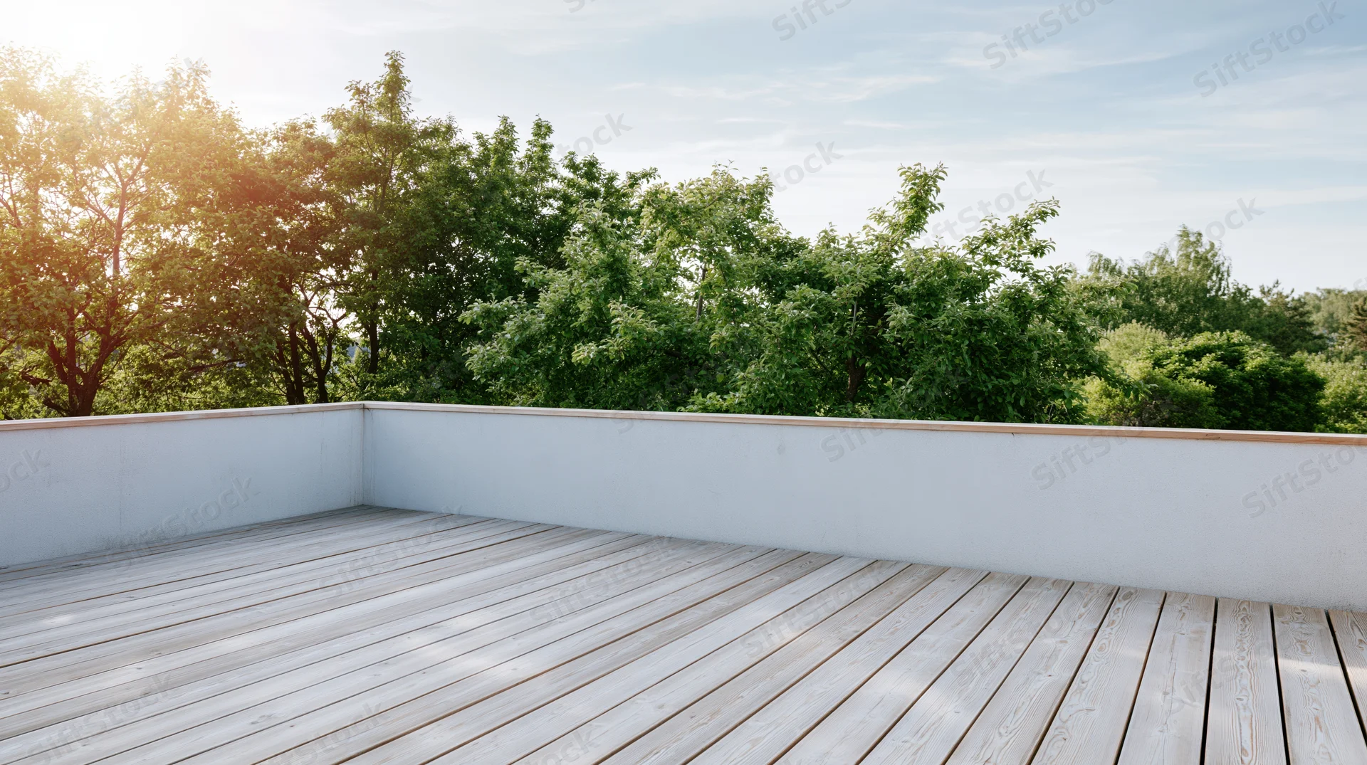 Empty wooden deck terrace with bleached planks overlooking green trees under morning sunlight